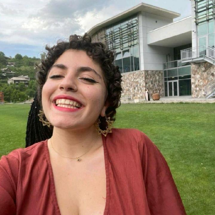 Karni in a red dress, smiling during their high school graduation.
