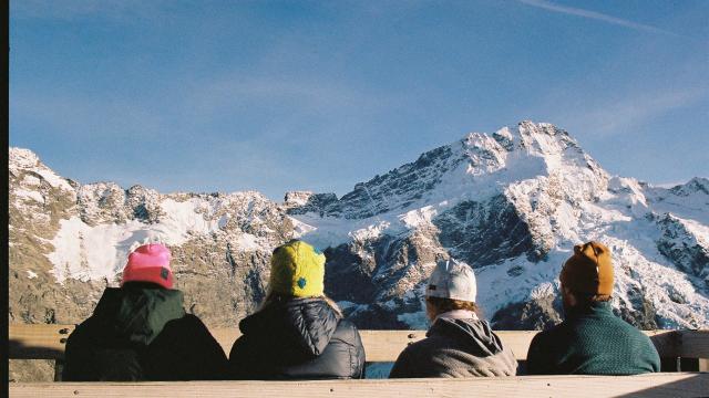 Four people sitting on a bench with the view of Mount Cook in front of them. 
