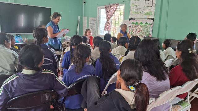 A group of school-aged girls from the Little Sisters fund program standing up one by one giving self- introductions. The program manager, co-founder, and I are in the background. 