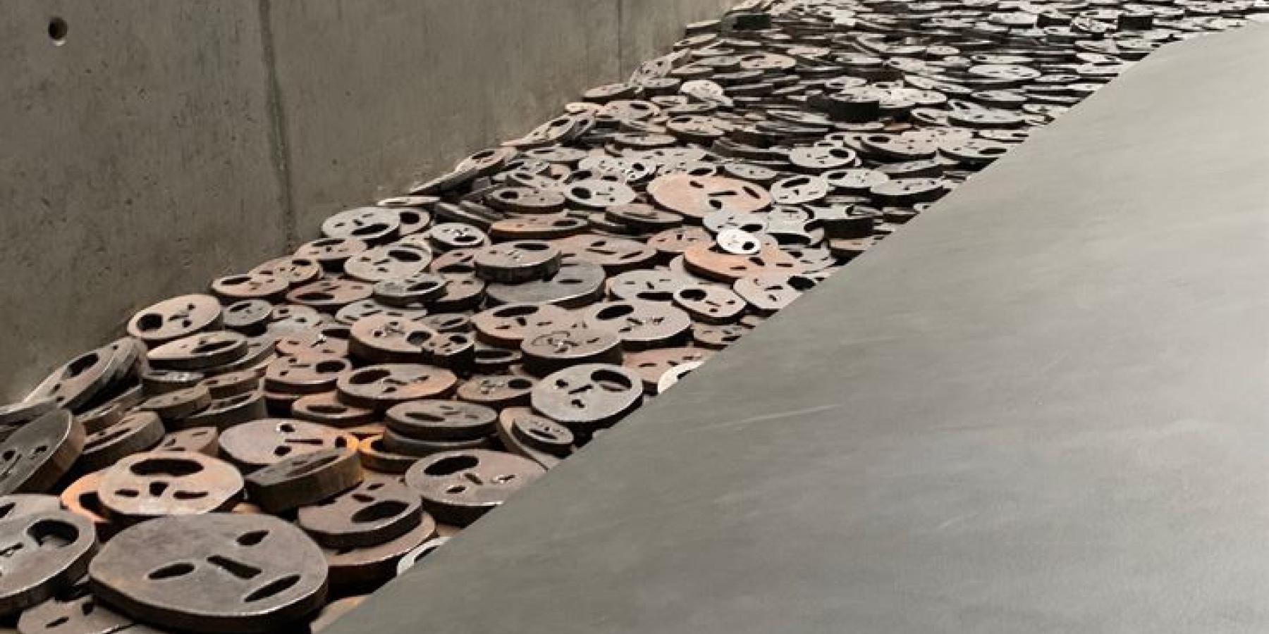 A hallway within a museum. Metal two-dimensional faces lay on the floor.