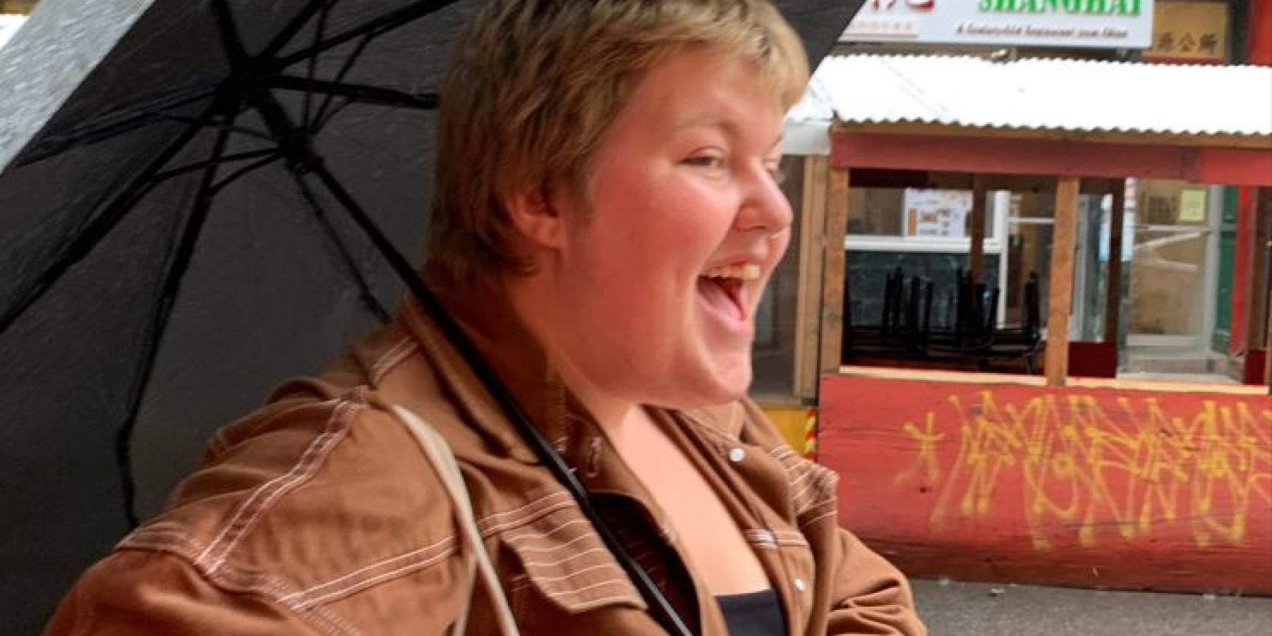 Sara walks in a New York City street with an umbrella.