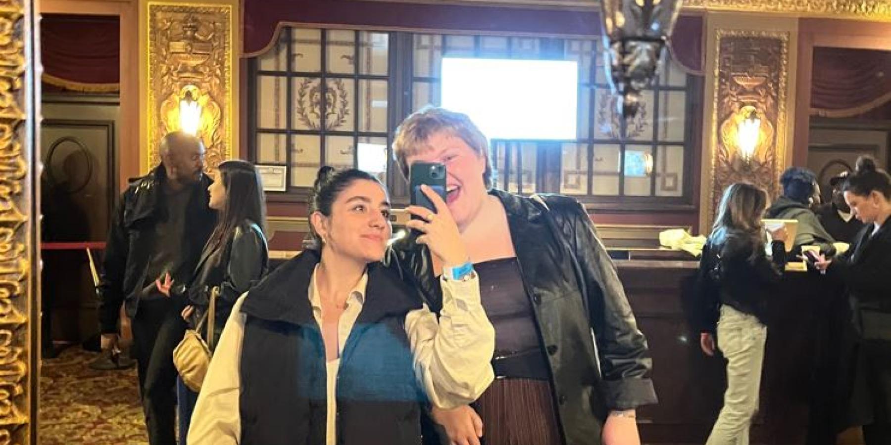 Sara and a friend take a selfie in front of a mirror.