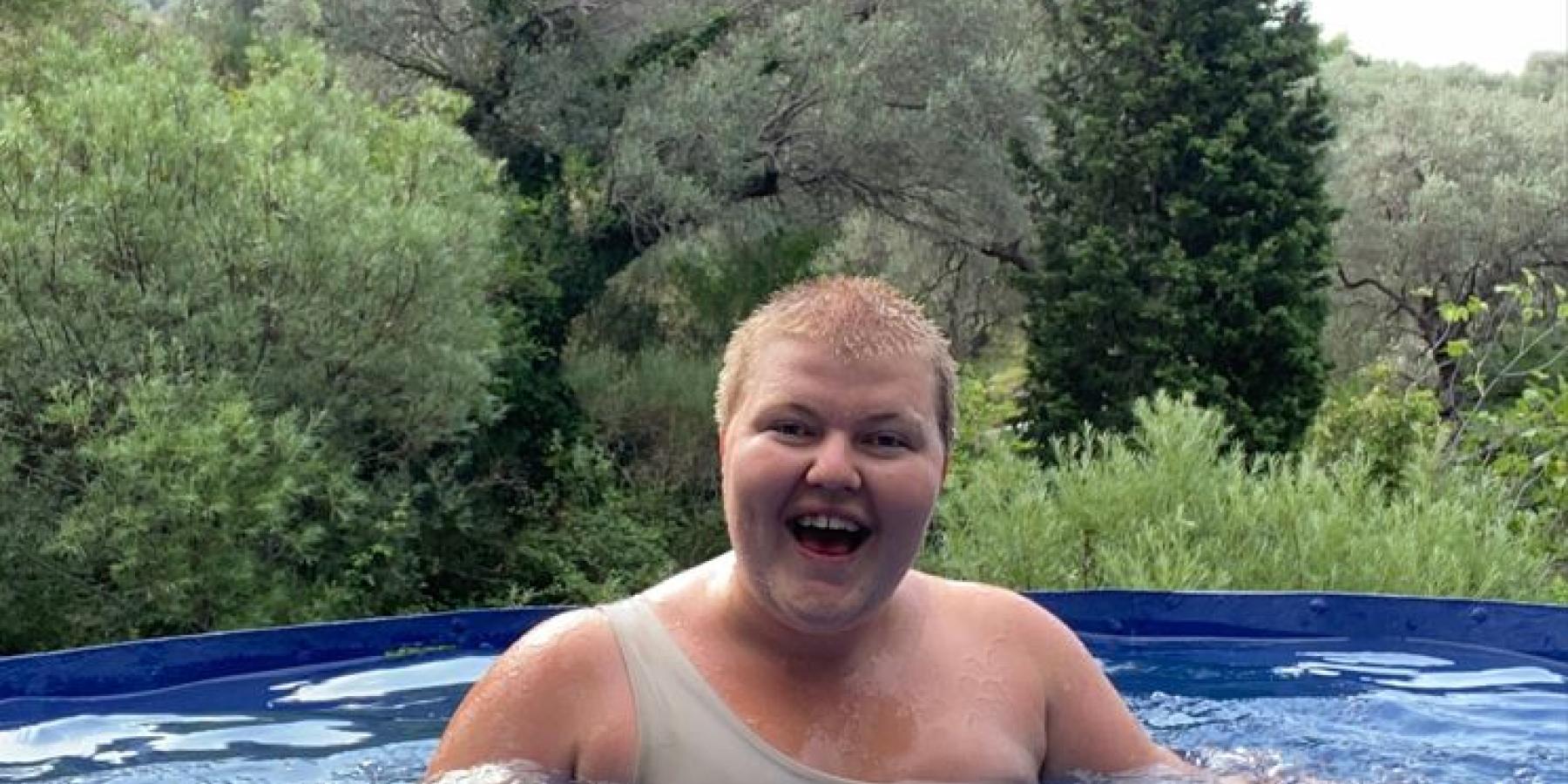 Sara stands in a outdoor pool surrounded by forest.