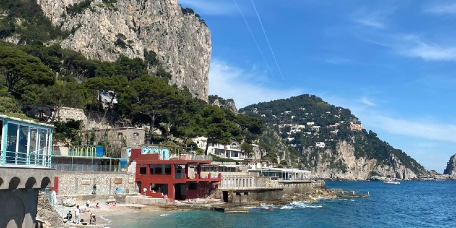 Photo of buildings and a mountain alongside bright blue ocean water.