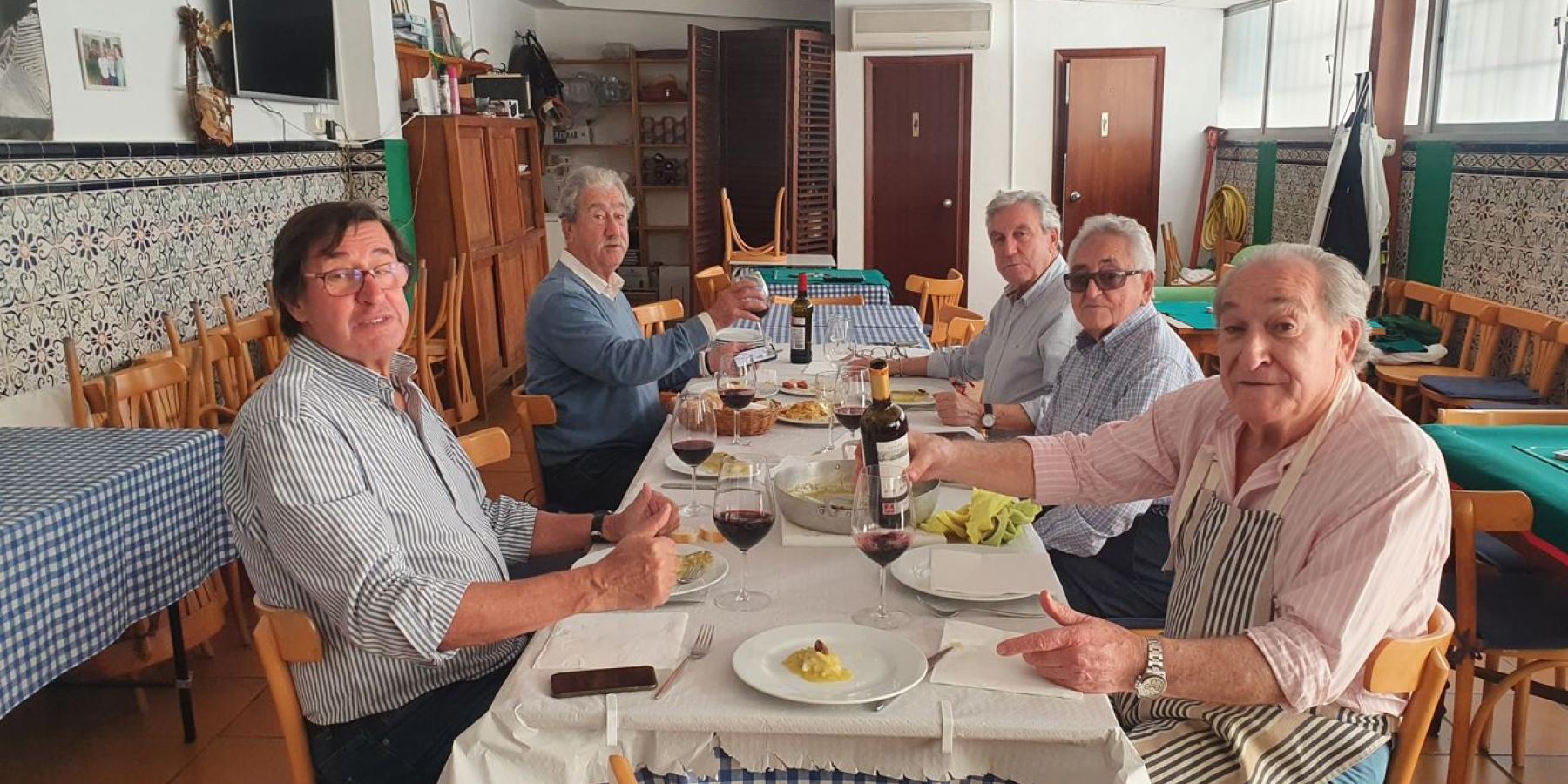 A group of five men sit around a table with glasses of wine.