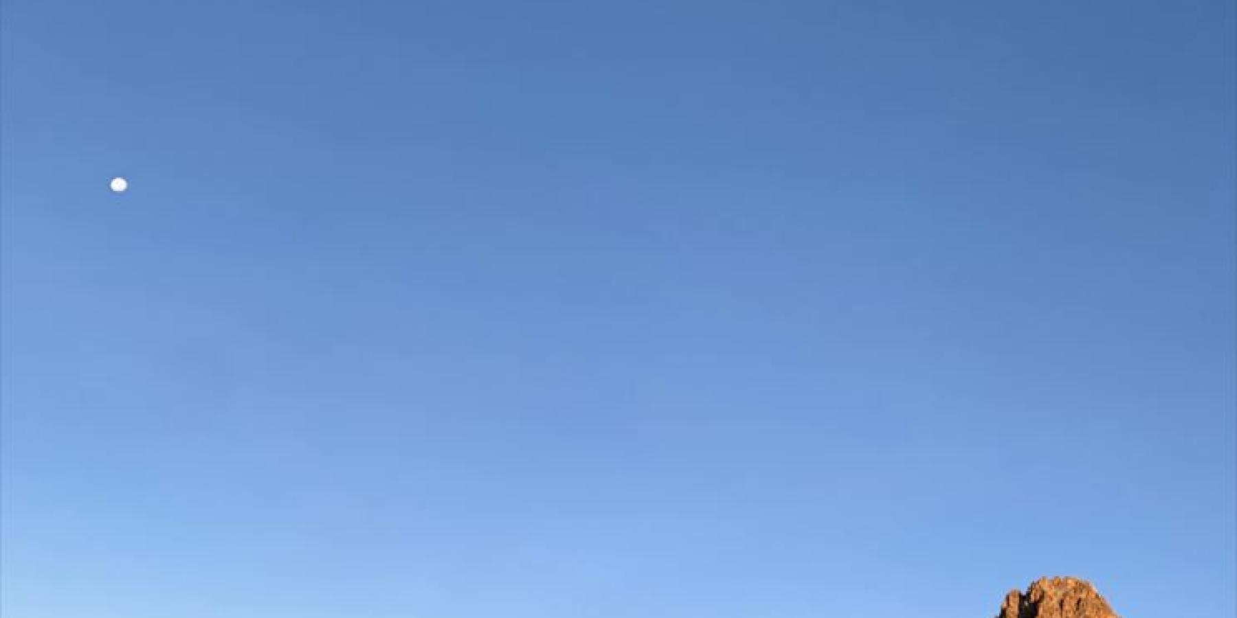 Sunlight bounces off of red rocks against a blue sky.