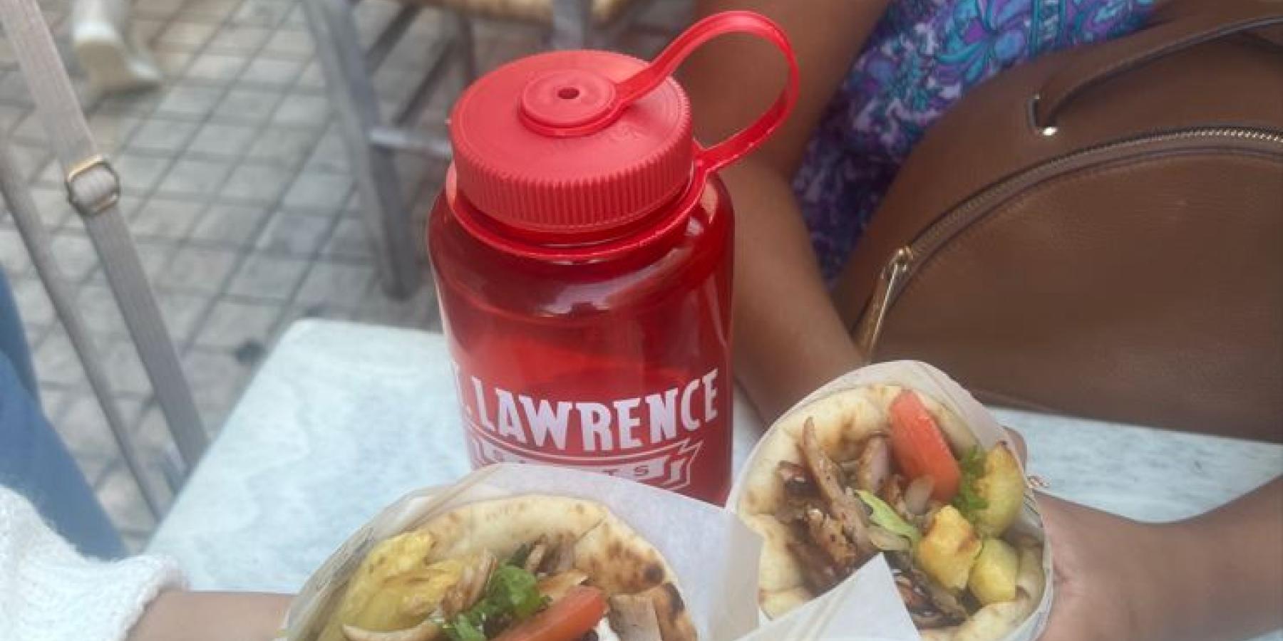 Three students hold pitas filled with meat and vegetables. A red St. Lawrence water bottle sits in the background.