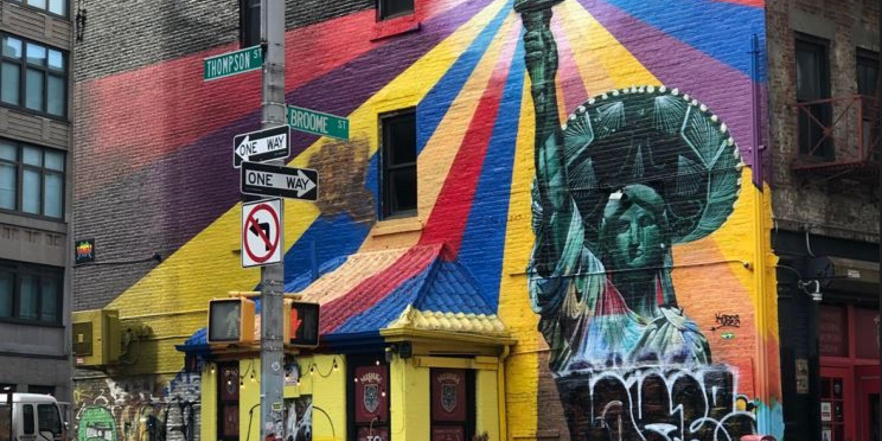 Street art depicting the statue of liberty wearing a sombrero with rainbows emanating from her torch.