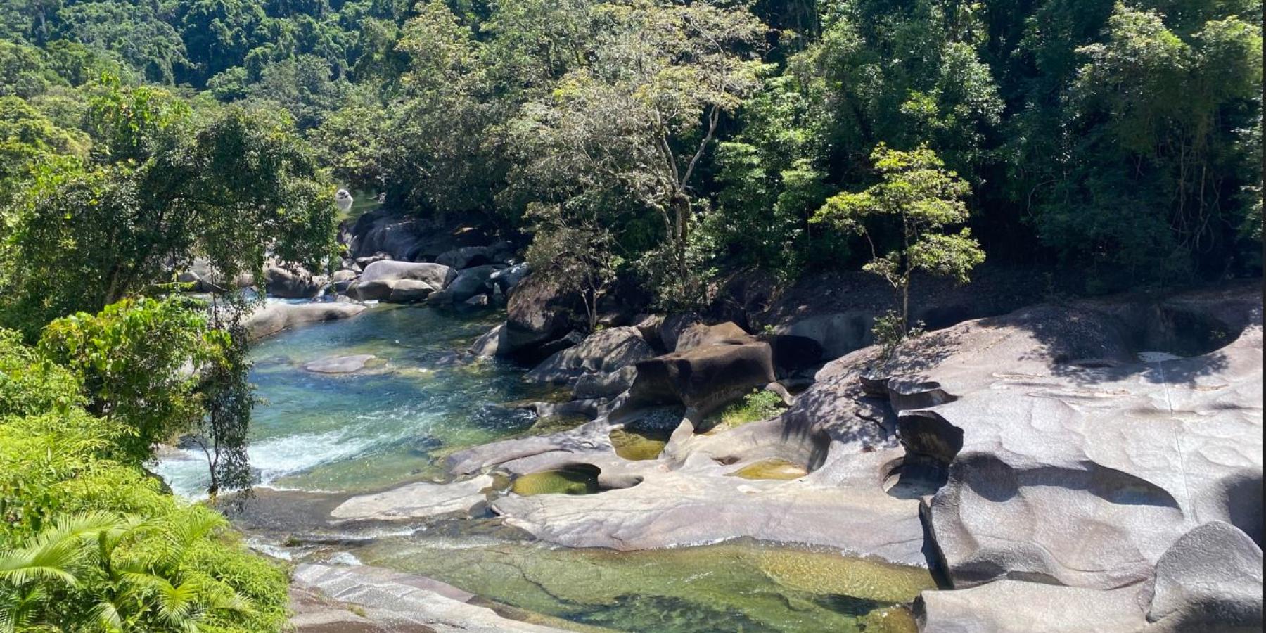 A river flows through rocks and into a bright blue pool of water.