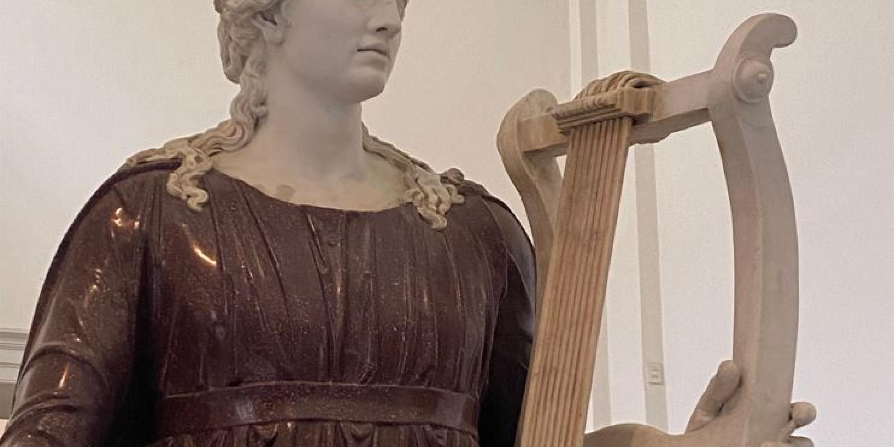 A statue of a woman wearing a burgundy robe and holding a harp.