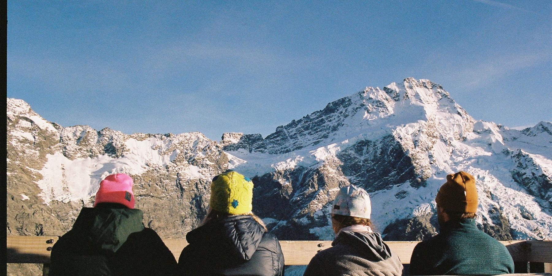 Four people sitting on a bench with the view of Mount Cook in front of them.
