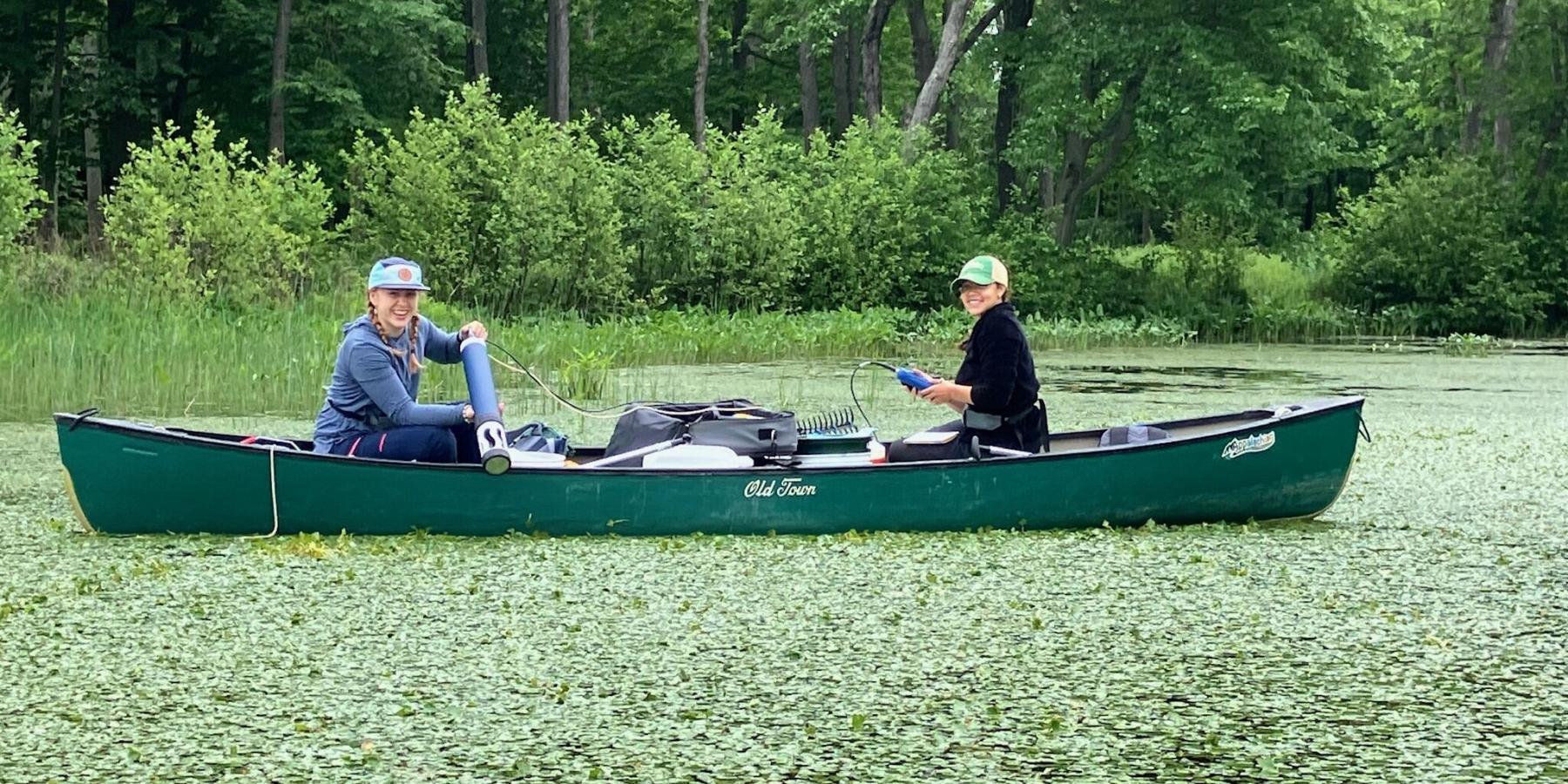 Students using lab equipment from a canoe in a river filled with vegetation