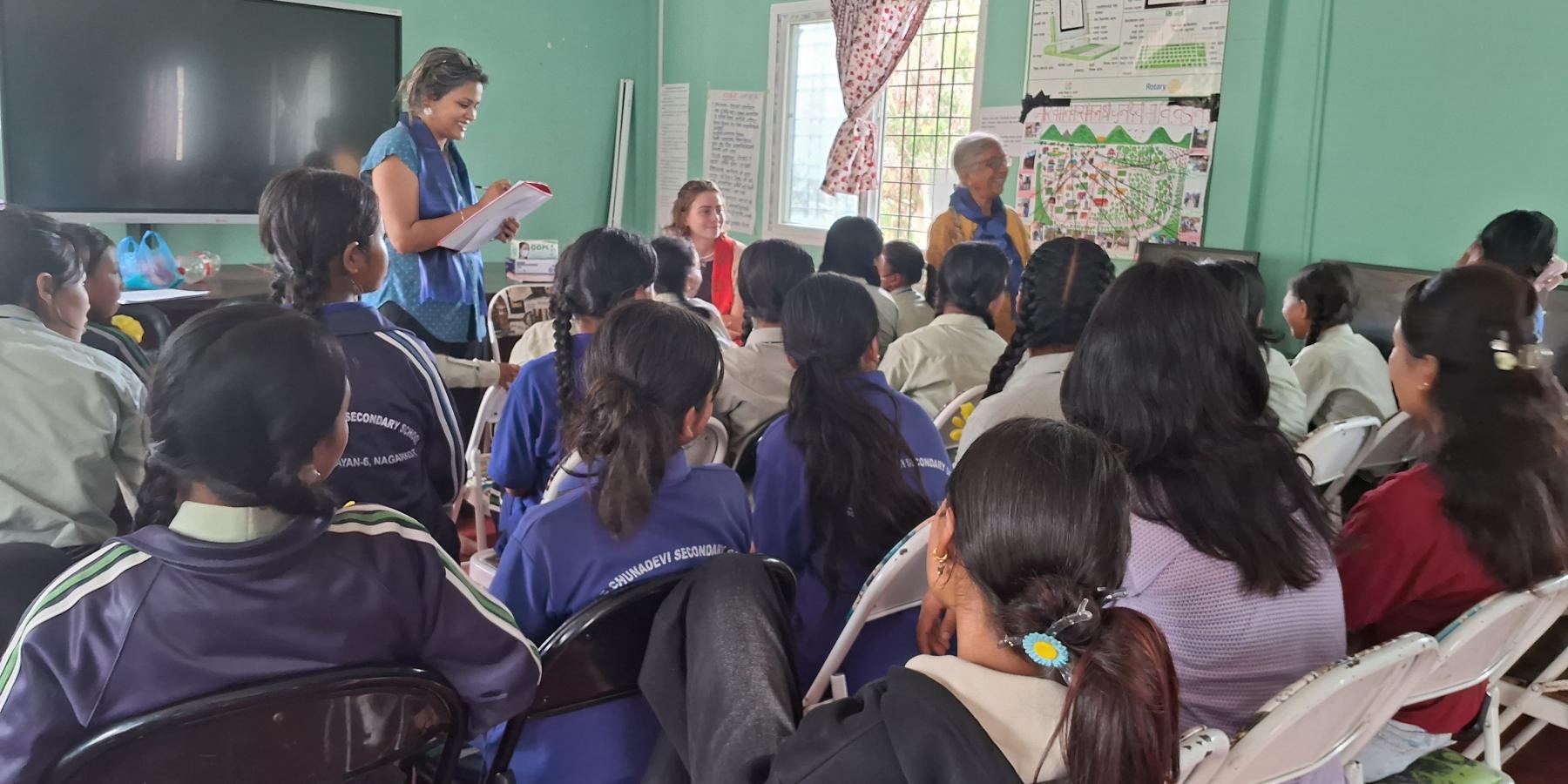 A group of school-aged girls from the Little Sisters fund program standing up one by one giving self- introductions. The program manager, co-founder, and I are in the background.