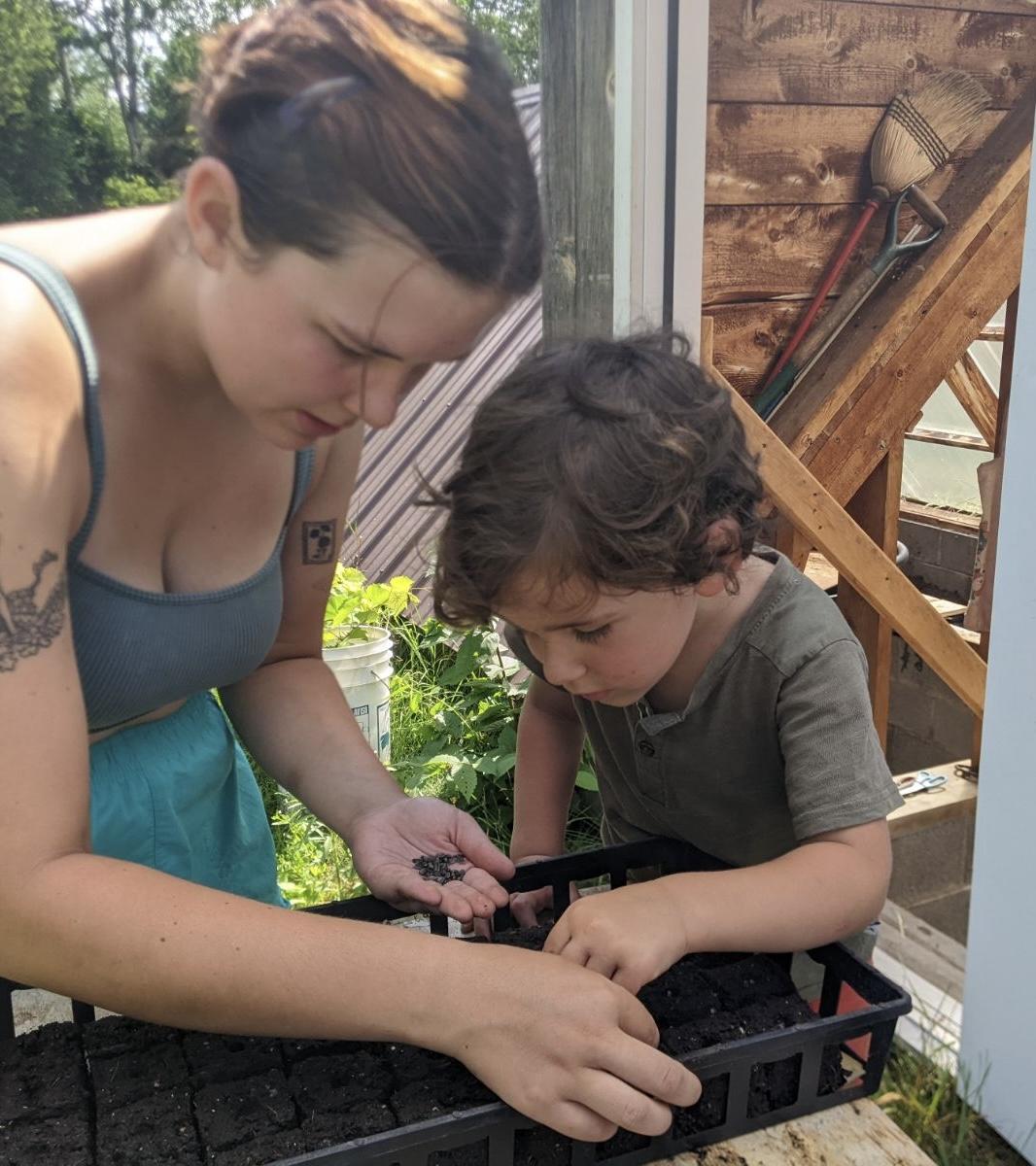 A girl and a little boy bent over a seed box planting melon seeds. 