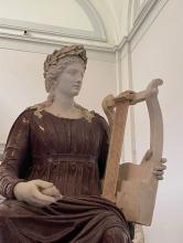 A statue of a woman wearing a burgundy robe and holding a harp.