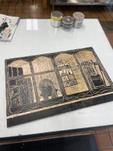 woodblock with image carved and covered in black in on a glass table