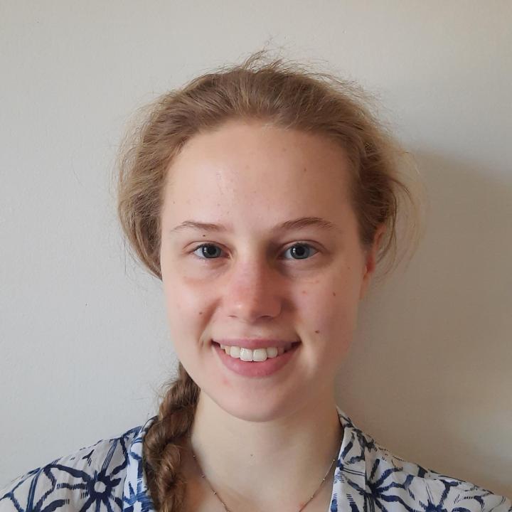 Image of a young woman smiling, with blond hair in a braid and a white collared shirt with blue star-like patterns.