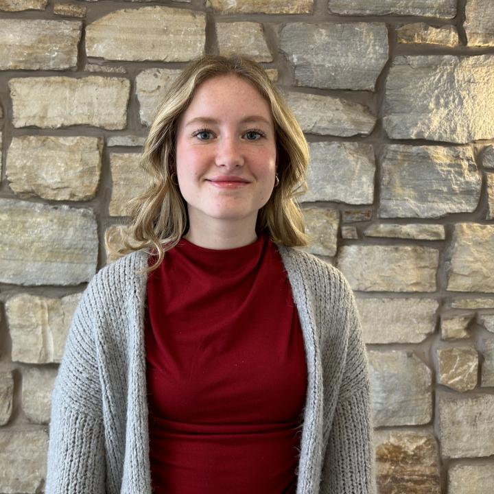 Image of blonde woman wearing red shirt standing in front of stone wall.