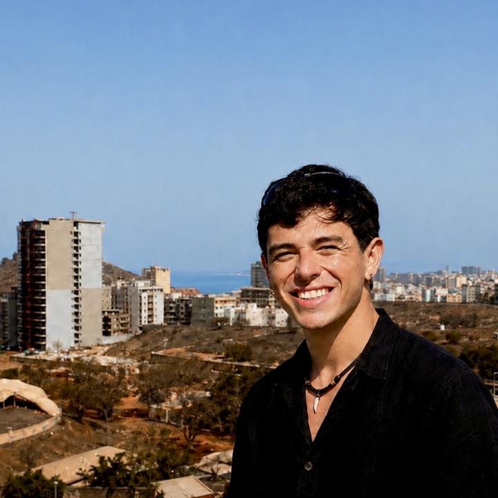 Picture smiling on the balcony next to African Renaissance Monument overlooking the downtown of Dakar, Senegal, with the cityscape and Atlantic Ocean visible in the background.