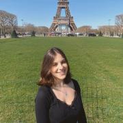 Gabriela stands in front of the Eiffel Tower and smiles.