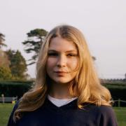 Photo of blonde woman with a dark shirt on while outside. 
