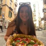 Sophia smiles while showing off a pizza in Italy.