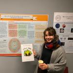Alexandria stands in a coat and scarf next to her poster displaying her research.