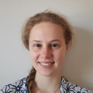 Image of a young woman smiling, with blond hair in a braid and a white collared shirt with blue star-like patterns.
